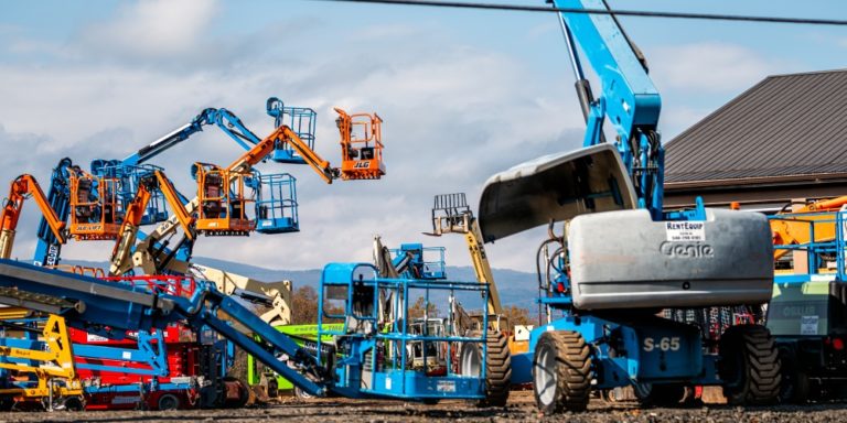 Variety of boom lifts sit in an equipment rental yard.