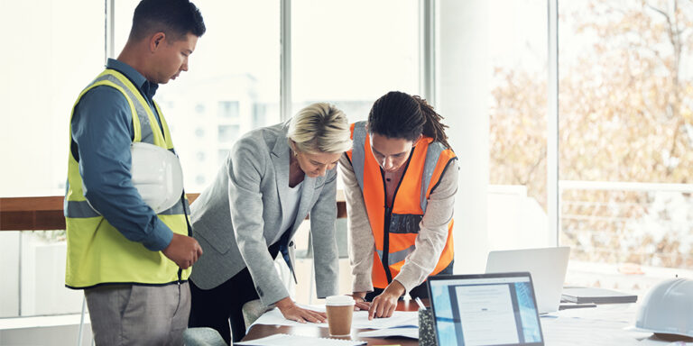 3 construction workers in an office looking at documents on a desk