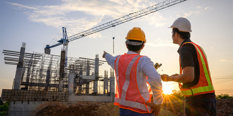2 construction professionals pointing towards an unfinished jobsite structure as the sun sets.