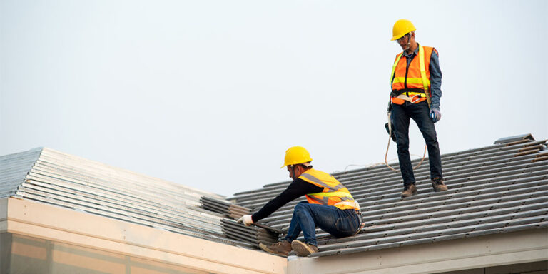 Two roofing specialty contractors working on top of a roof