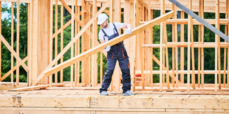 Worker lifting a beam to build wood frame construction at a jobsite