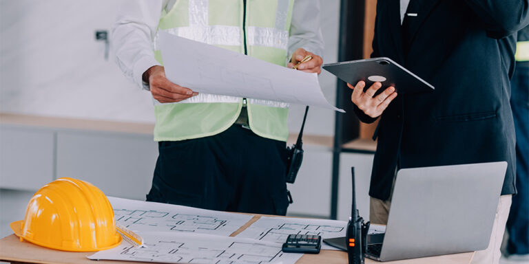 Two workers illustrating construction progress tracking through paper documents and tablet for collecting and sharing project information.