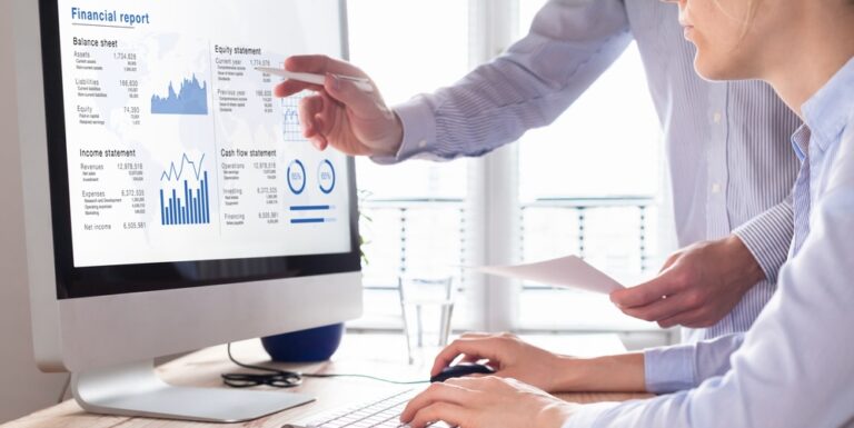 Two people looking at different financial measurement reports on a desktop computer