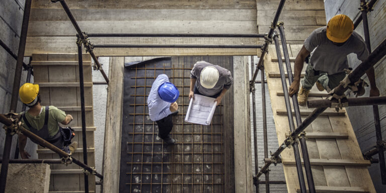 Overhead view of two construction workers construction workers viewing site plans on a construction site.