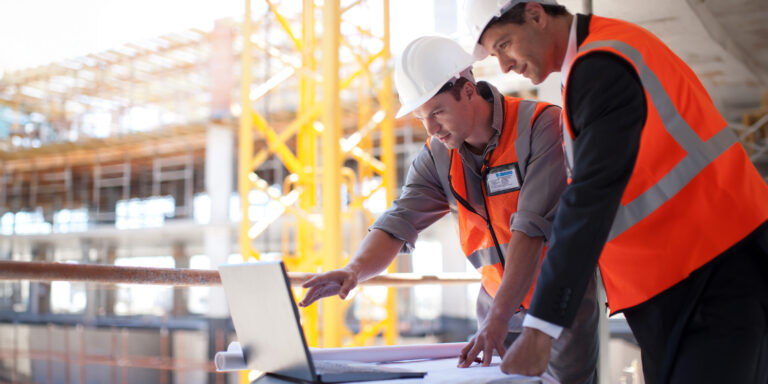 Two construction workers looking at a laptop on a jobsite