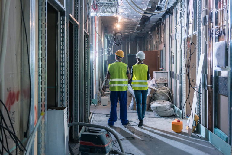 2 people in the wall of a building under construction conducting a mechanical rough-in inspection