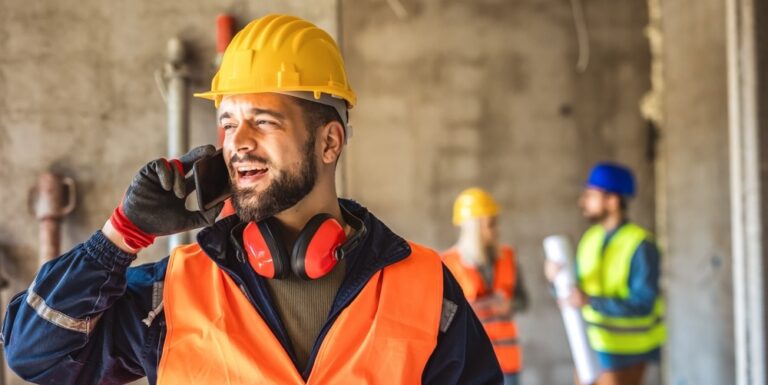 Construction communication on site illustrated by worker using their phone with other workers