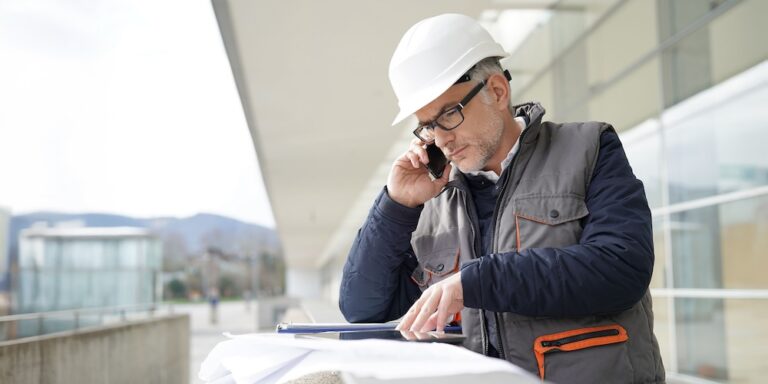 Construction quality control manager taking a phone call while reviewing documents